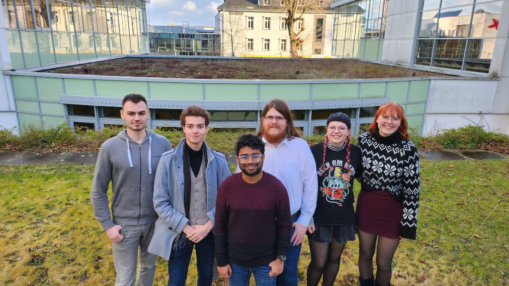 Sechs Personen stehen vor einem Gebäude: Justin, Bryan, Adari, Marc, Juliana und Emma (Myriele ist nicht anwesend).